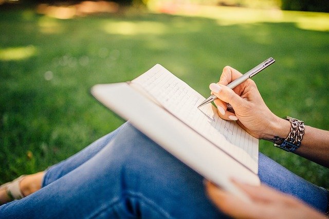 good writer writing story in notebook on grass daytime