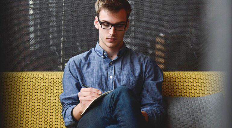 man sitting on couch with his pen and paper to write down his ideas